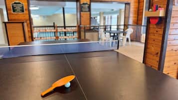 Une table de ping-pong avec une raquette et une balle, dans une pièce aux murs en bois, donnant sur un balcon.