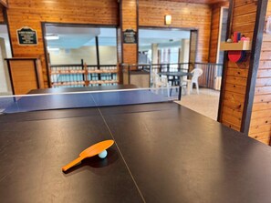 A ping pong table with a paddle and ball in a room with wooden walls and a view of a balcony.