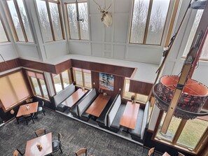 Un restaurant avec de hauts plafonds, de grandes fenêtres et un espace central aménagé avec des banquettes et des tables.