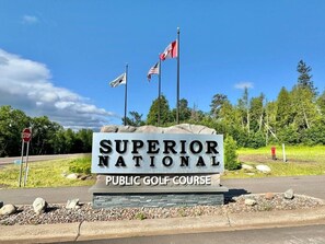 Señal del campo de golf público nacional Superior con dos banderas, una señal de stop y un cielo despejado.