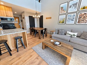A modern kitchen with a granite countertop, black stools, and a dining area with a wooden table and chairs.