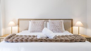 Un lit bien fait, recouvert d’une couverture moelleuse, avec deux oreillers et deux lampes de chevet posées sur des tables de nuit en bois.