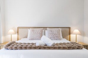 Ein ordentlich bezogenes Bett mit einer flauschigen Decke, zwei Kissen und je einem Nachttisch mit einer Nachttischlampe.