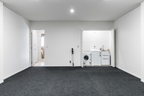 Ein Zimmer mit grauem Teppich, weißen Wänden, einer Waschmaschine und einem Staubsauger.