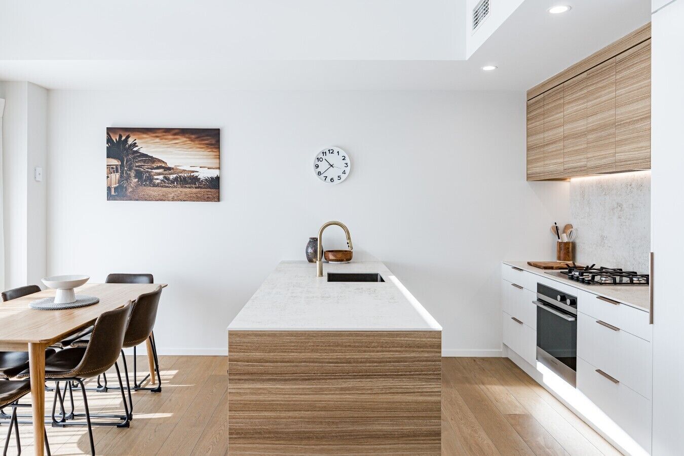 A modern kitchen with a central island, a dining area with a table and chairs, and a clock on the wall.