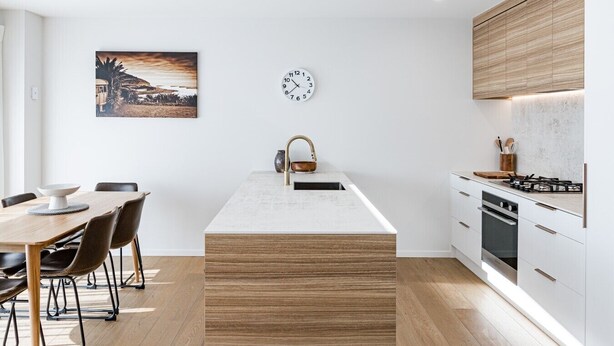 Une cuisine moderne avec un îlot central, un coin repas comprenant une table et des chaises, et une horloge au mur.