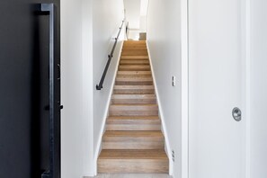 Ein schmaler Flur mit einer Holztreppe, die zu einer Tür mit einer silbernen Klinke führt.