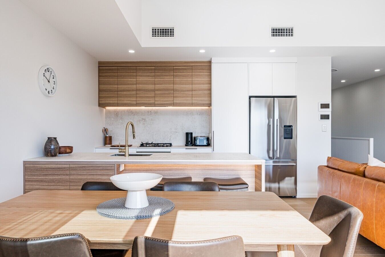 Een moderne keuken met een centraal eiland, roestvrijstalen apparatuur en een eetgedeelte met een houten tafel en lederen stoelen.