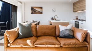 Un salon moderne avec un canapé en cuir, un coin repas et une cuisine dotée d’un plan de travail en bois.