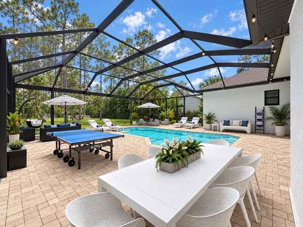 An outdoor patio with a pool, lounge chairs, a ping pong table, and a covered seating area.