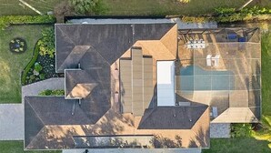 Luchtbeeld van een modern gebouw met een geometrisch dakontwerp, een zwembad en aangelegde tuinen.