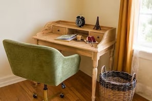 Un escritorio de madera con cajones, una silla verde, una cesta de mimbre y una pequeña reproducción de la Torre Eiffel.