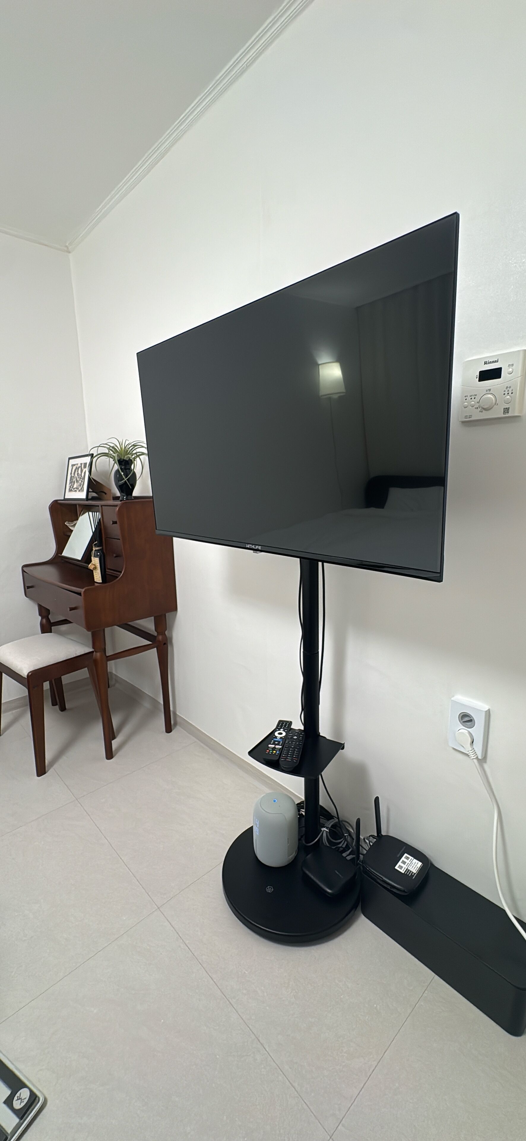 A flat-screen TV mounted on a stand, a wooden desk with a chair, and a small table with a plant.