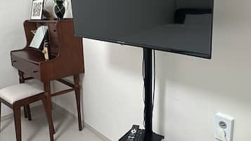 A flat-screen TV mounted on a stand, a wooden desk with a chair, and a small table with a plant.