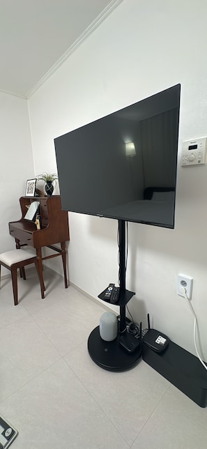 A flat-screen TV mounted on a stand, a wooden desk with a chair, and a small table with a plant.
