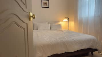 A bedroom with a bed, a door, a wall-mounted picture, and a bedside lamp.
