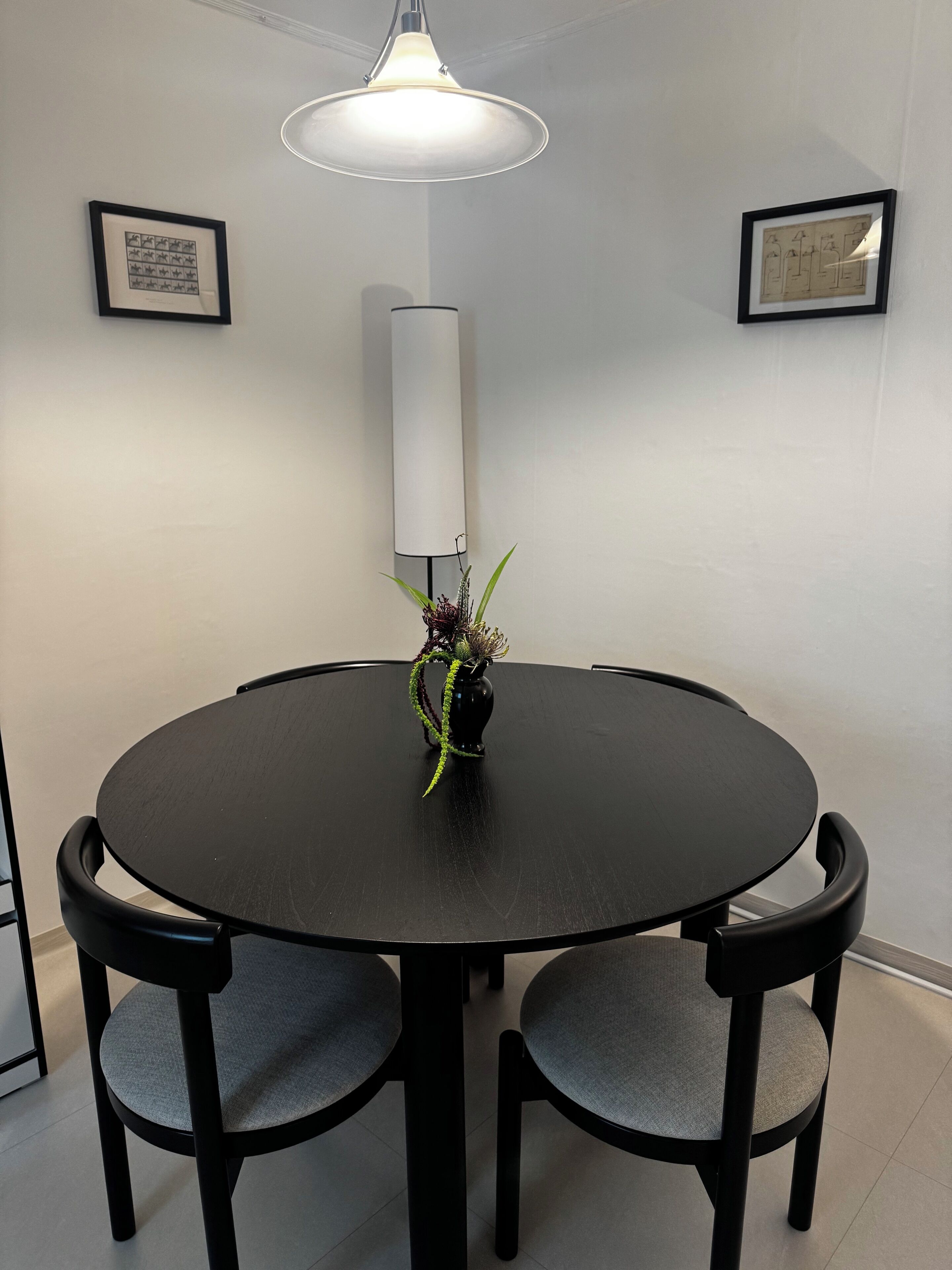 A round dining table with four chairs, a vase with a plant, and two framed artworks on the wall.