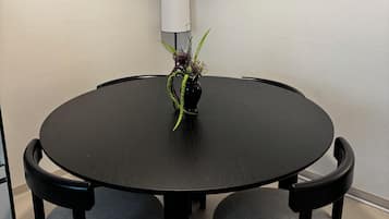 A round dining table with four chairs, a vase with a plant, and two framed artworks on the wall.