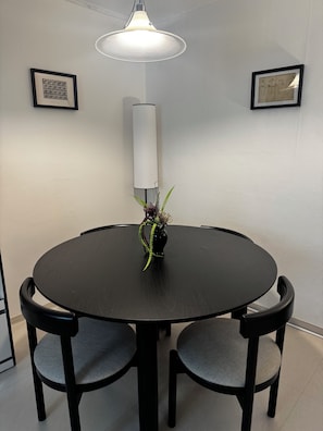A round dining table with four chairs, a vase with a plant, and two framed artworks on the wall.