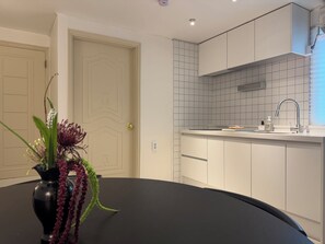 A modern kitchen with white cabinets, a black countertop, and a vase with flowers on the table. - 군자역3분 /성수/건대/KSPO/광화문/공항버스역3분/퀸침대3개/최대6인 (Seoul)