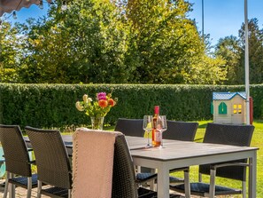 An outdoor dining area with a table set for two, surrounded by wicker chairs, a vase of flowers, and a bottle of wine. - "Rəzvan" -  from the sea by Interhome (Hadsund)