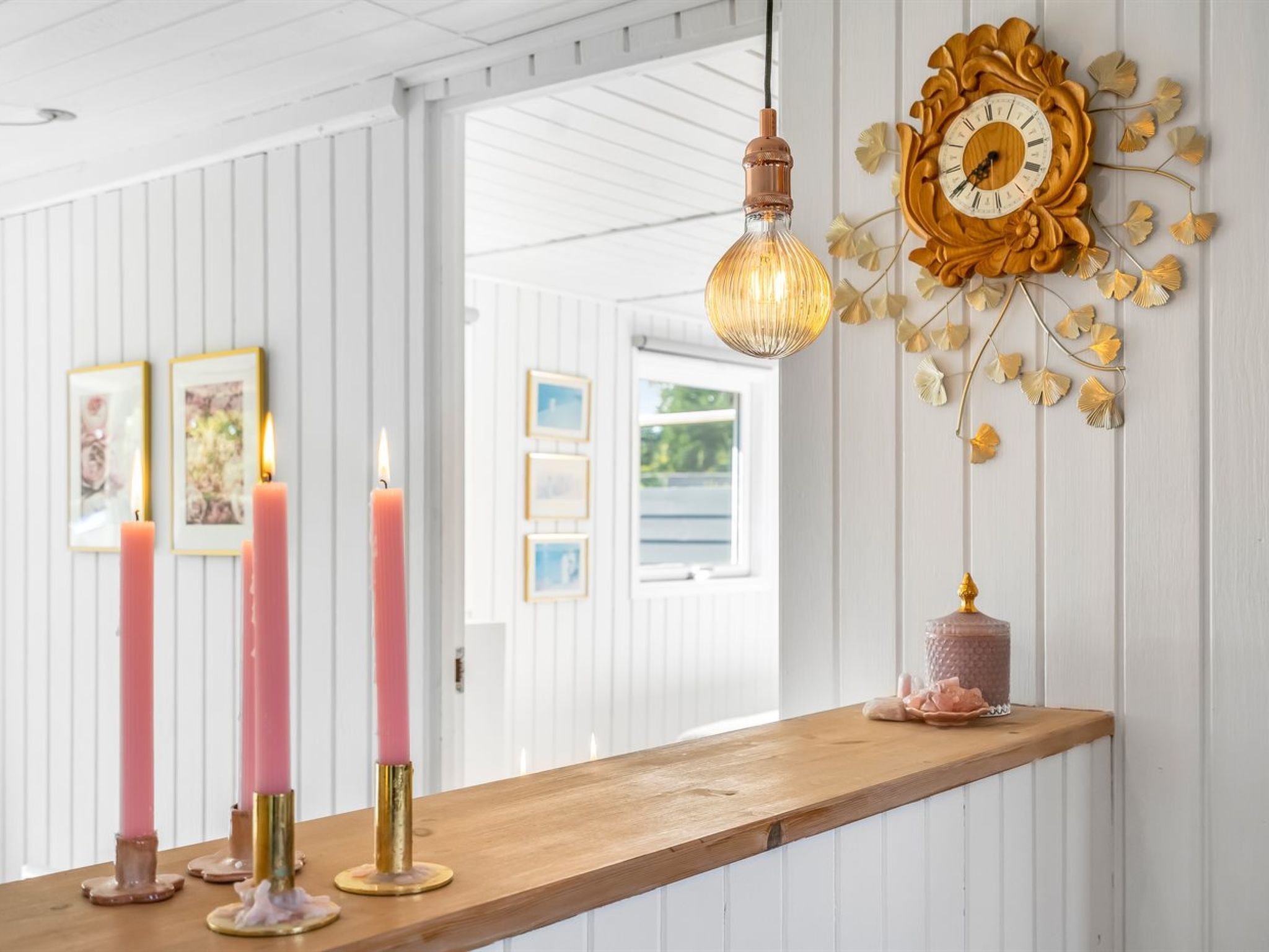 A room with a wooden bench, pink candles, a hanging light fixture, and a decorative wall clock.
