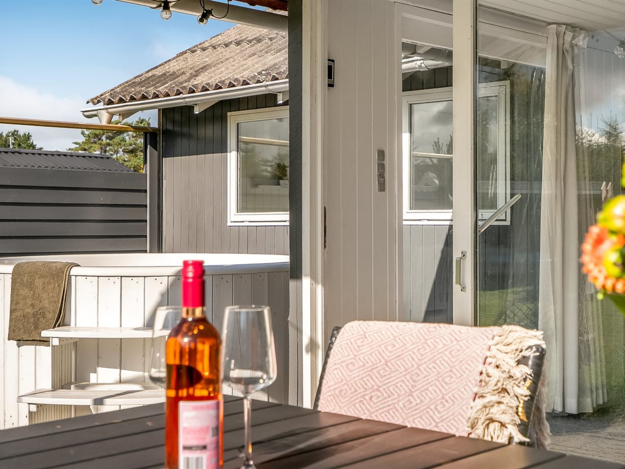 A covered outdoor seating area with a table, a bottle, and a glass.