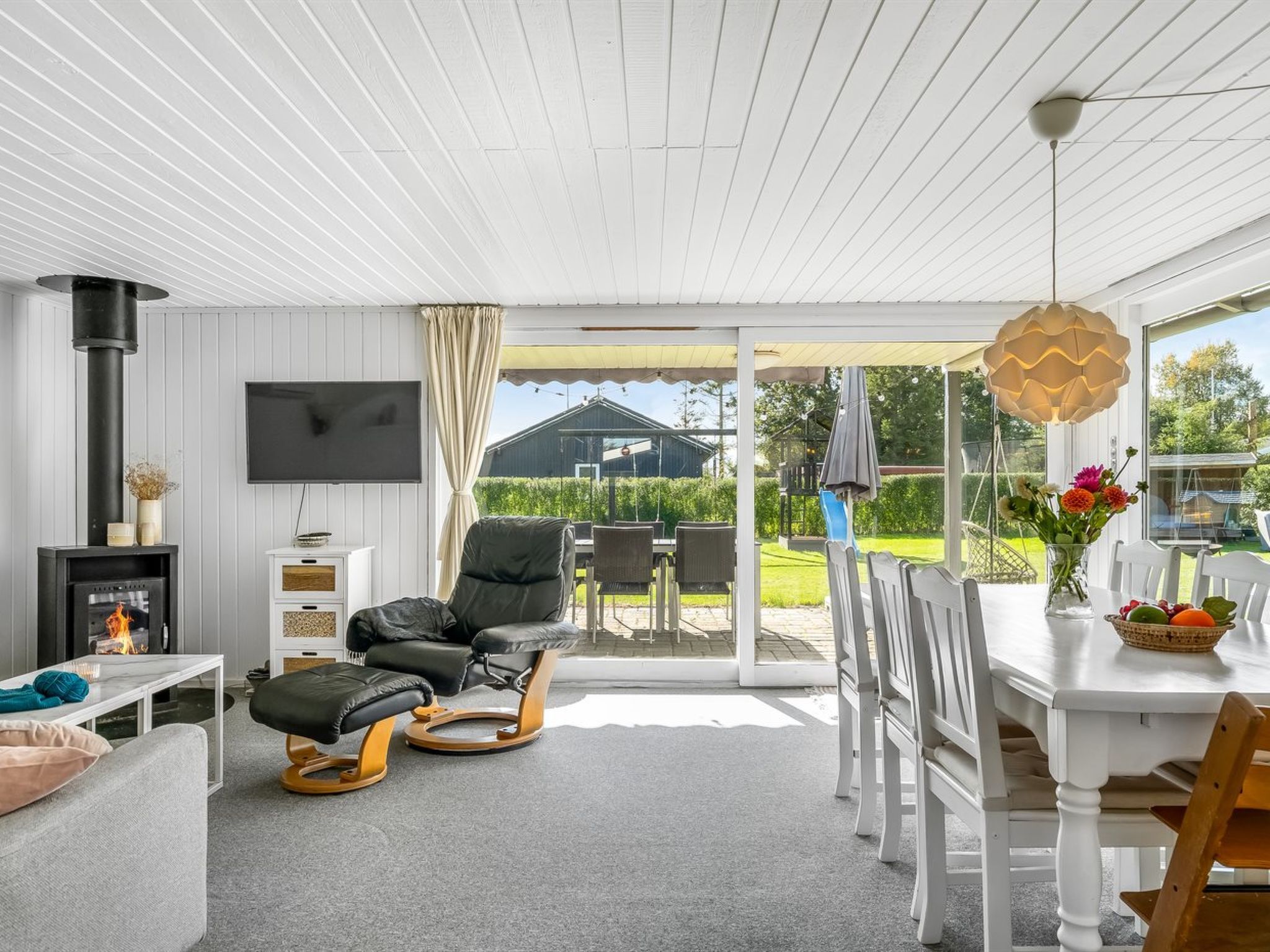 A modern living room with a fireplace, a television, and a dining area with a view of the outdoors.