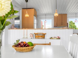 Cozinha com armários brancos, uma mesa de madeira com uma cesta de frutas e iluminação pendente.