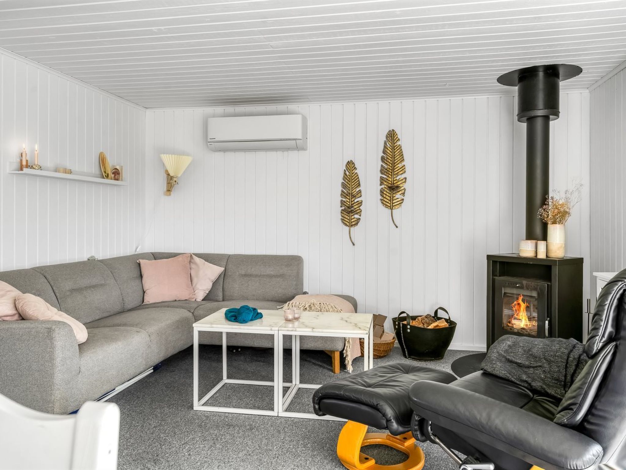 A modern living room with a grey sofa, a black leather chair, a white coffee table, and a fireplace with a black chimney.