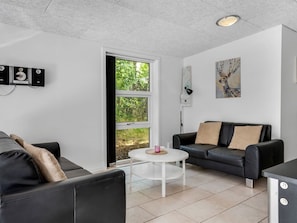 Ein modernes Wohnzimmer mit einem schwarzen Ledersofa, einem weißen Couchtisch und einer schwarzen Lederliege. Ein Fenster bietet Blick auf viel Grün draußen.