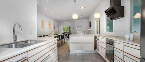 Une cuisine moderne dotée d’un îlot central, d’appareils électroménagers intégrés et de luminaires suspendus.