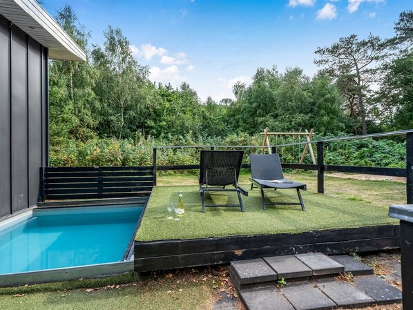 Ein Schwimmbecken mit einer Holzterrasse und zwei Liegestühlen.