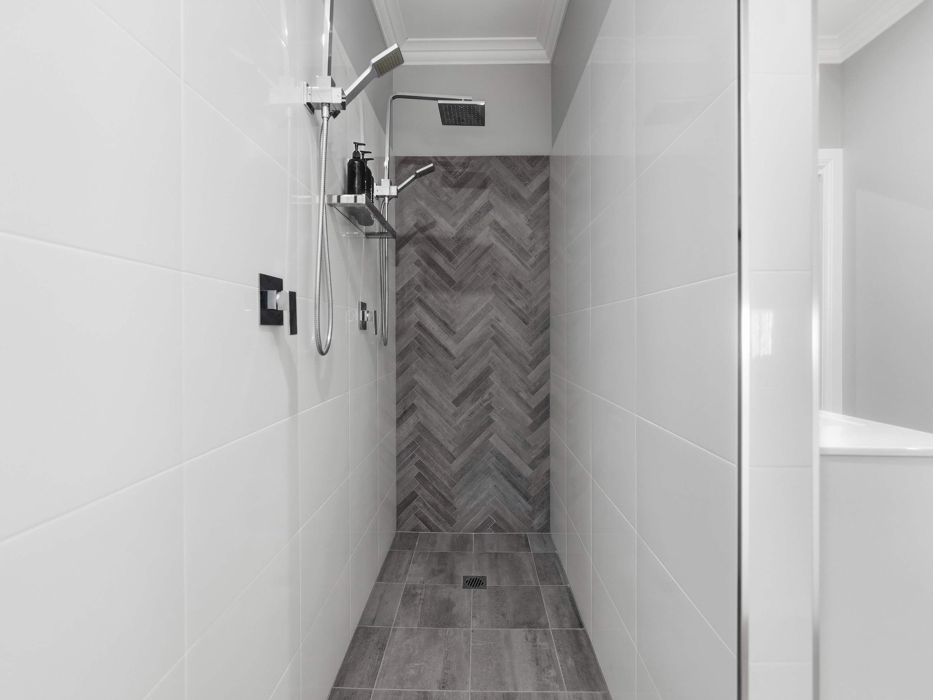 A modern shower with a herringbone-patterned wall, a chrome showerhead, and a handheld shower attachment.