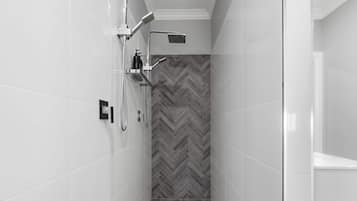 A modern shower with a herringbone-patterned wall, a chrome showerhead, and a handheld shower attachment.