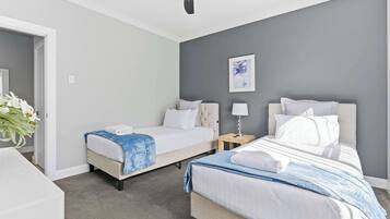 A hotel room with two beds, a ceiling fan, a bedside table with a lamp, and a framed artwork on the wall.