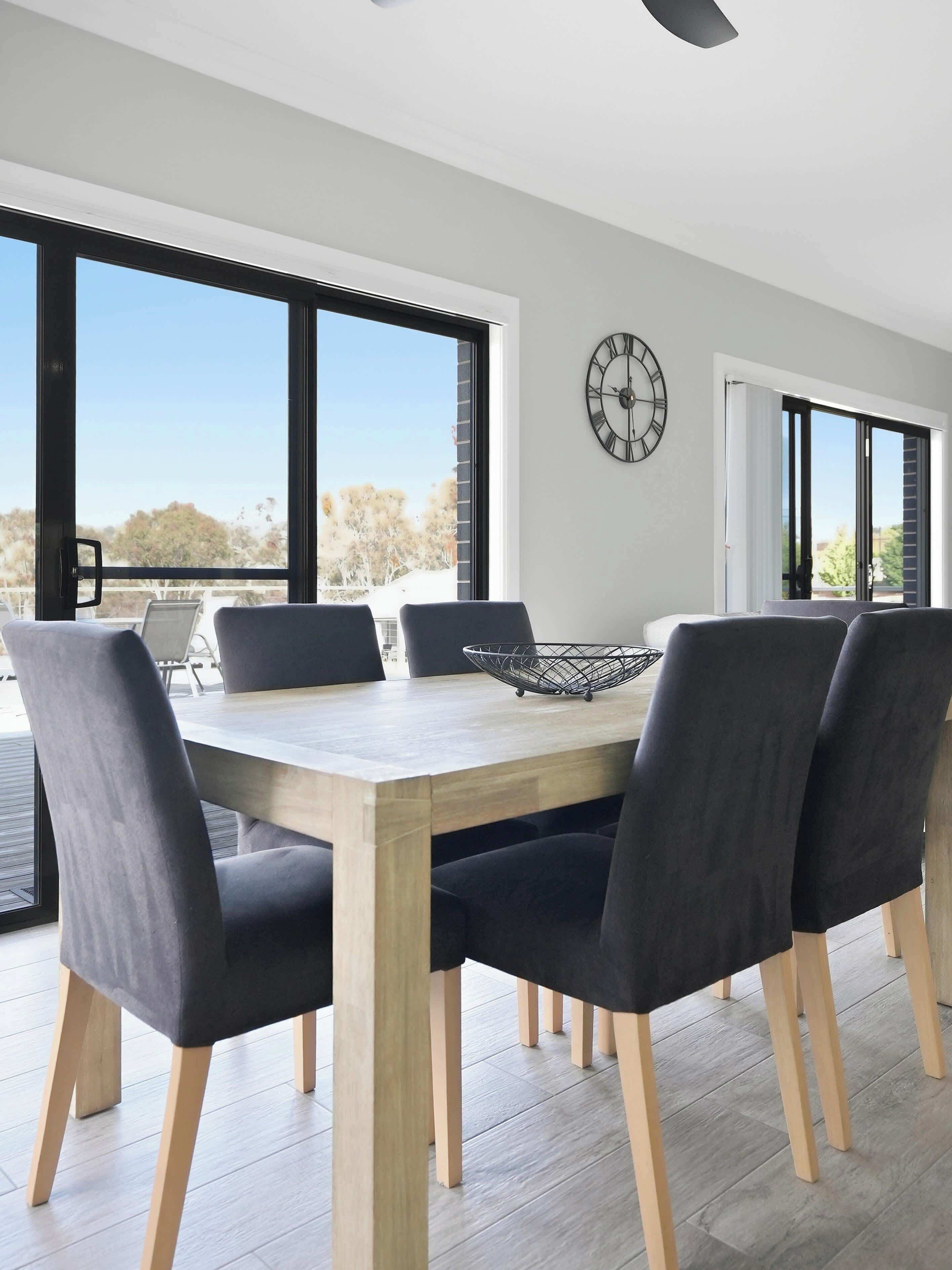 Un comedor moderno con una mesa de madera, sillas tapizadas en negro y un centro de mesa con un cuenco metálico.