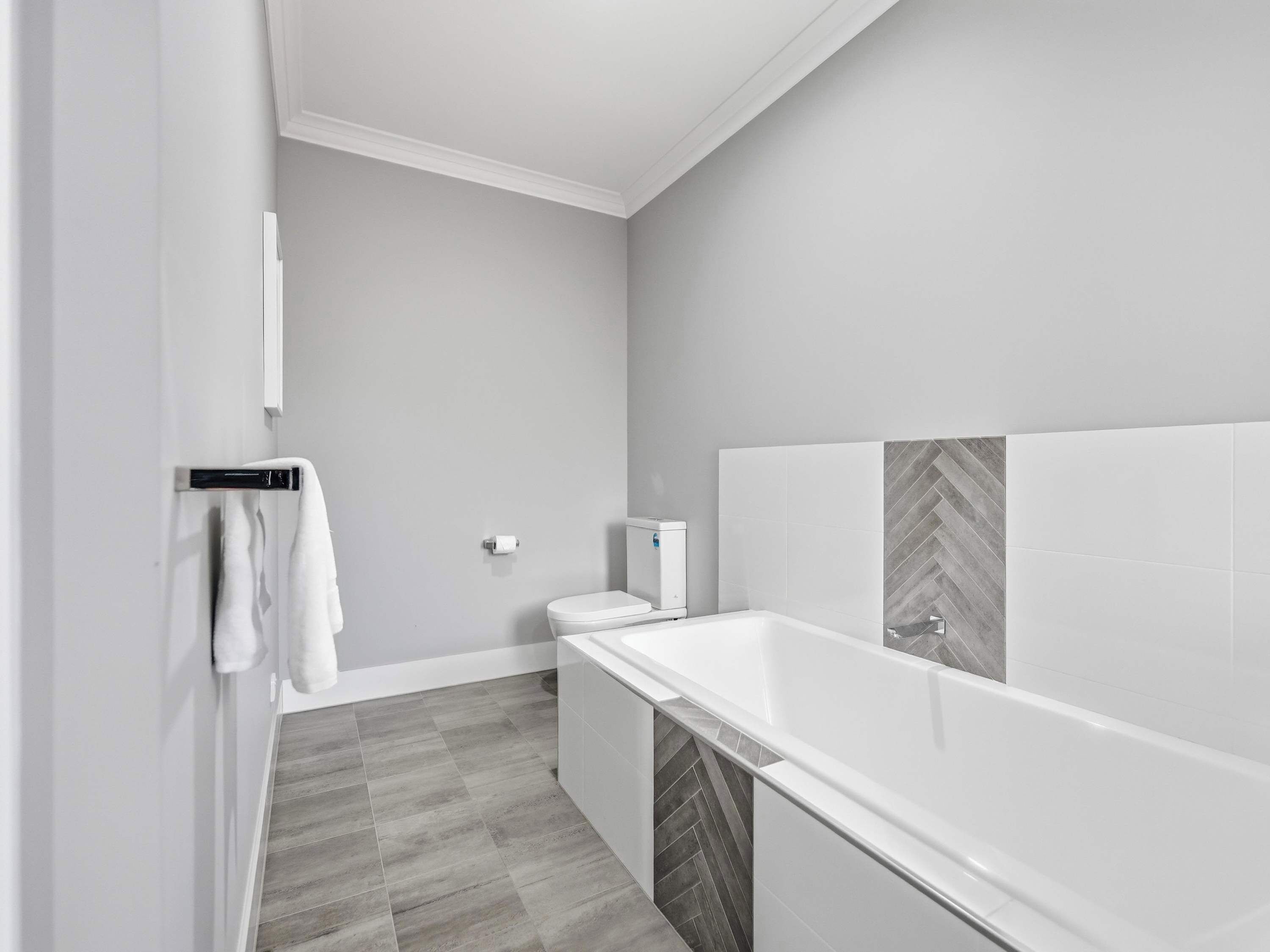 A modern bathroom with a white bathtub, grey herringbone-patterned tiles, and a toilet.
