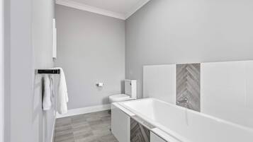 A modern bathroom with a white bathtub, grey herringbone-patterned tiles, and a toilet.