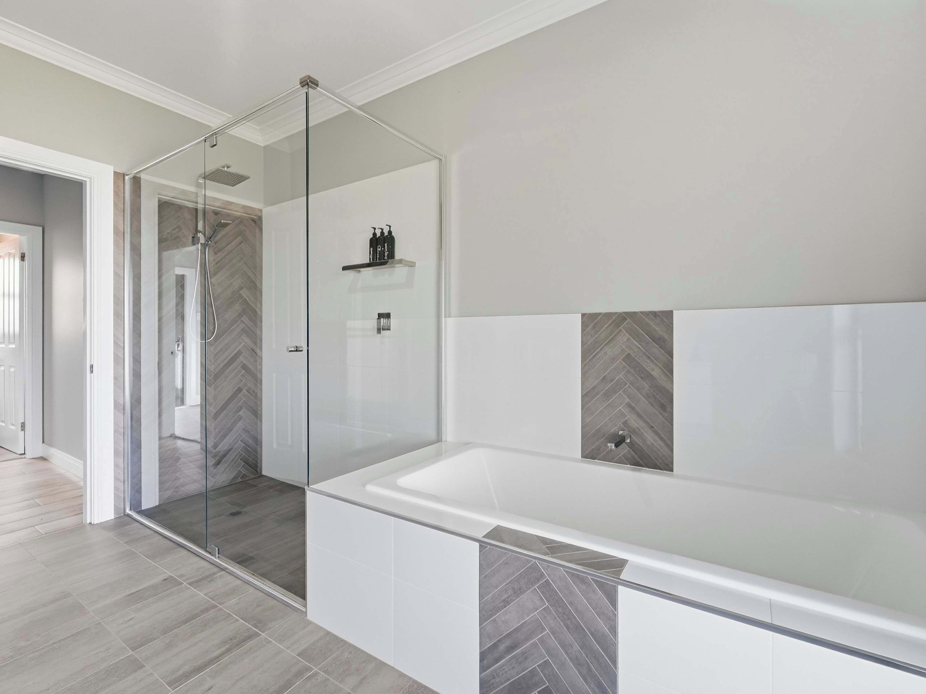 A modern bathroom with a glass-enclosed shower, a large white bathtub, and herringbone-patterned tiles.