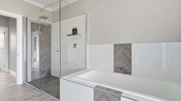 A modern bathroom with a glass-enclosed shower, a large white bathtub, and herringbone-patterned tiles.