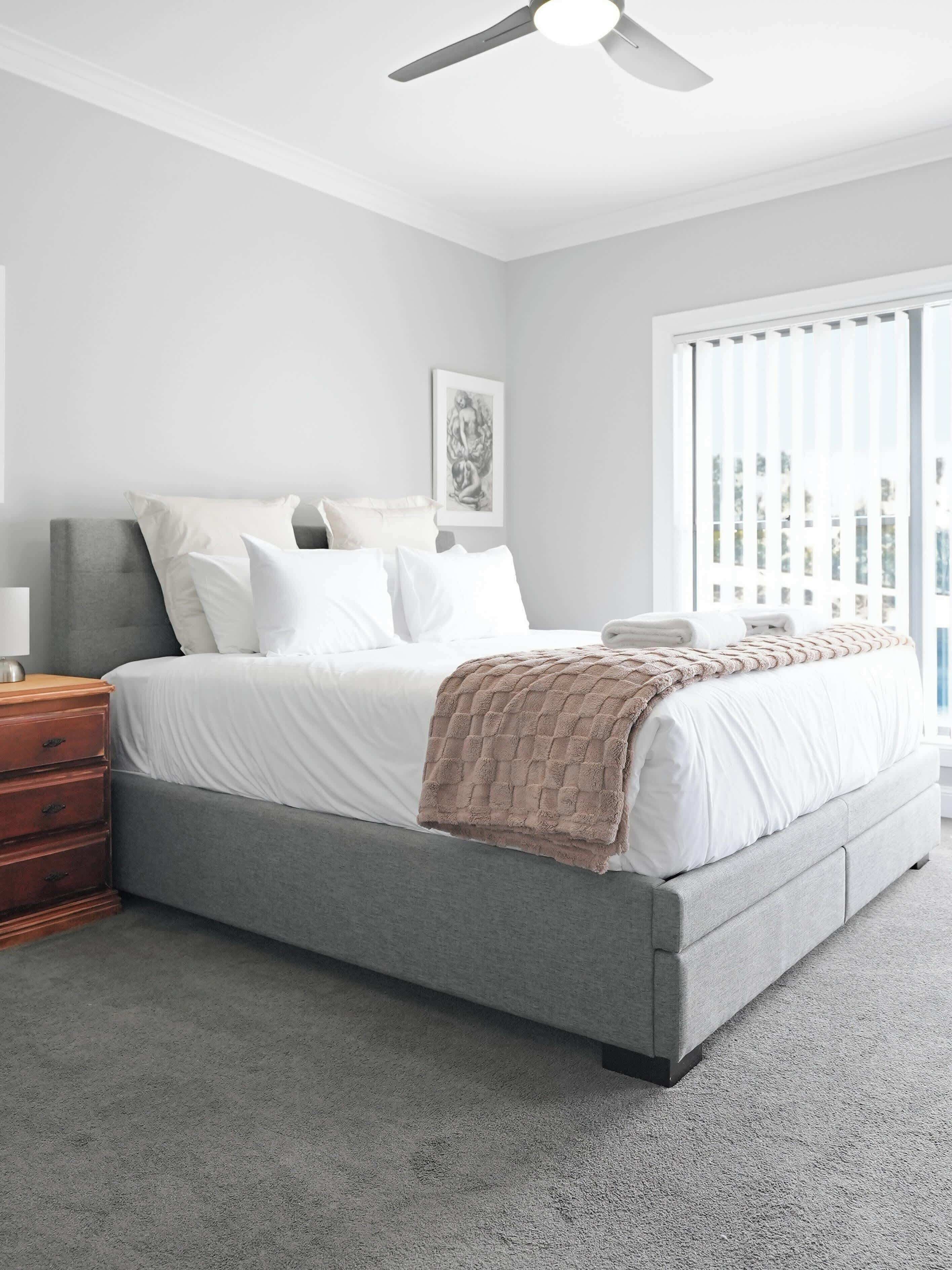 A bedroom with a bed, a nightstand, a dresser, a ceiling fan, and a window with blinds.