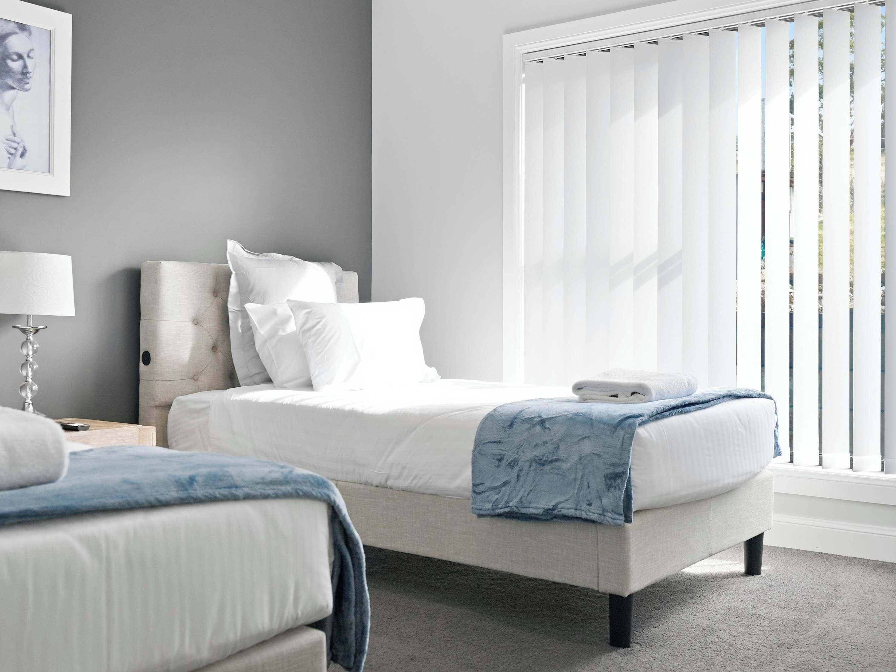 A bedroom with a bed, a nightstand, a lamp, and a window with blinds.