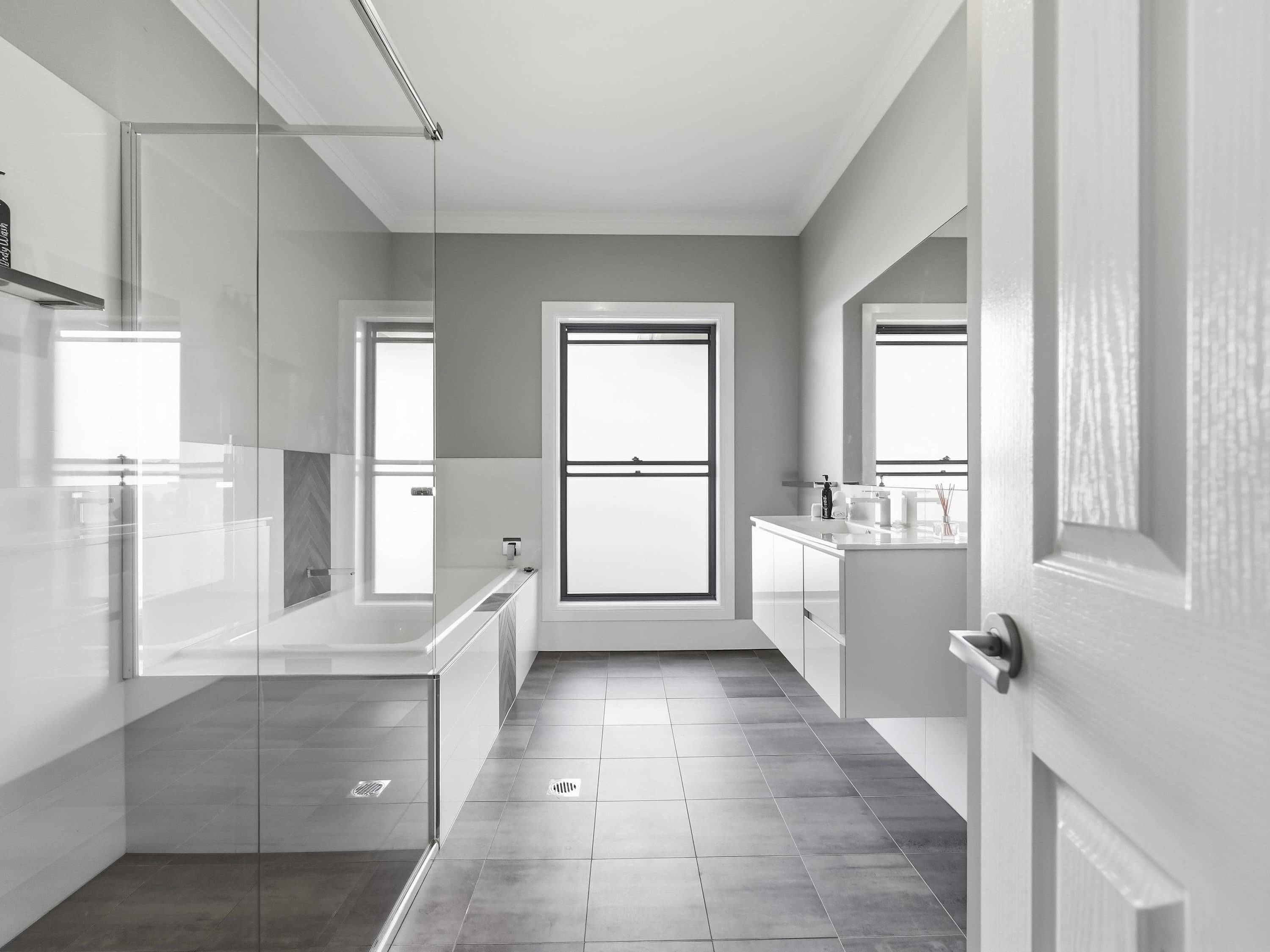 A modern bathroom with a glass shower enclosure, a white vanity, and a large window providing natural light.