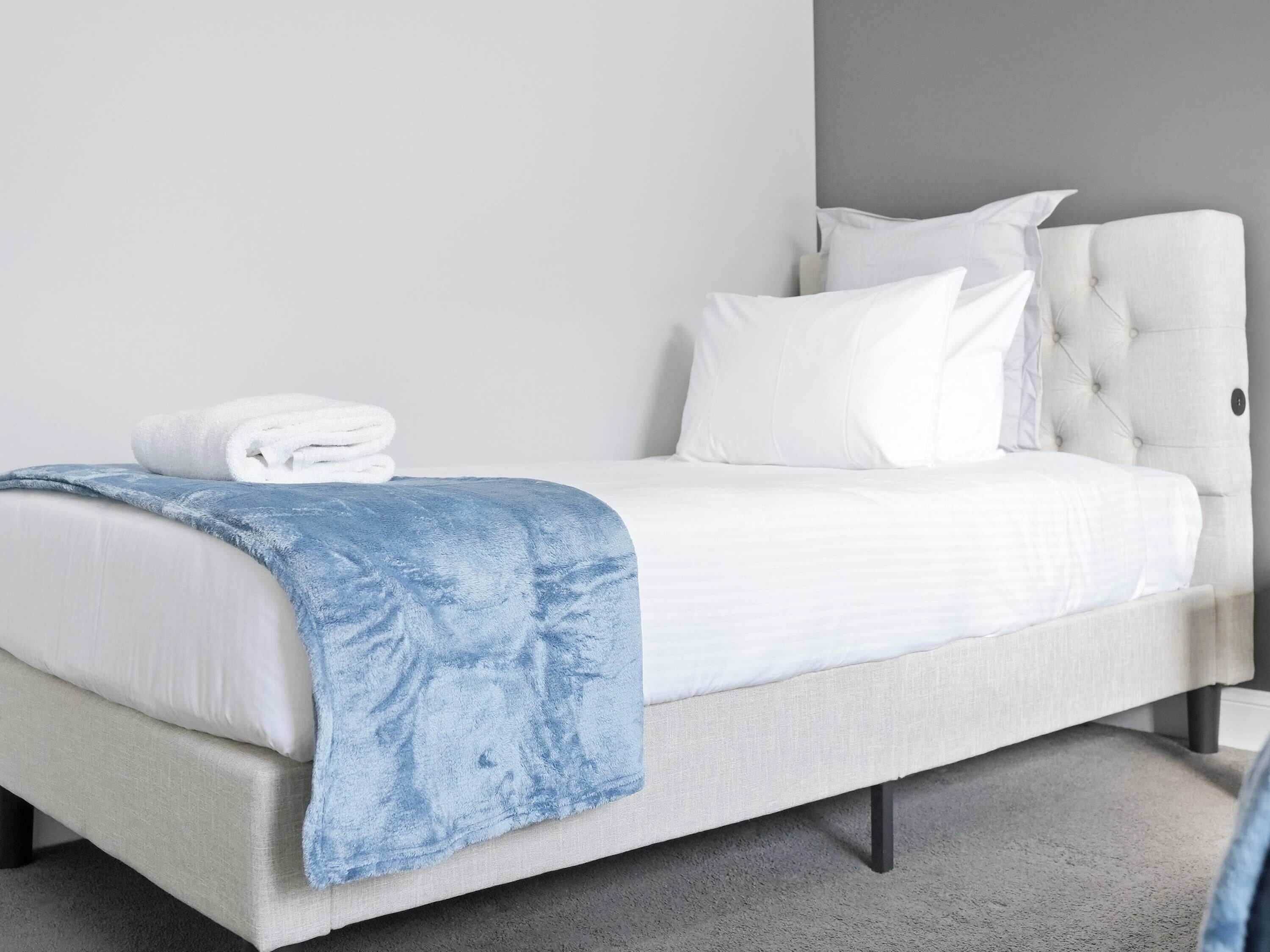 A bed with a white headboard, a blue blanket, and a stack of white towels.