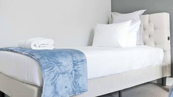 A bed with a white headboard, a blue blanket, and a stack of white towels.