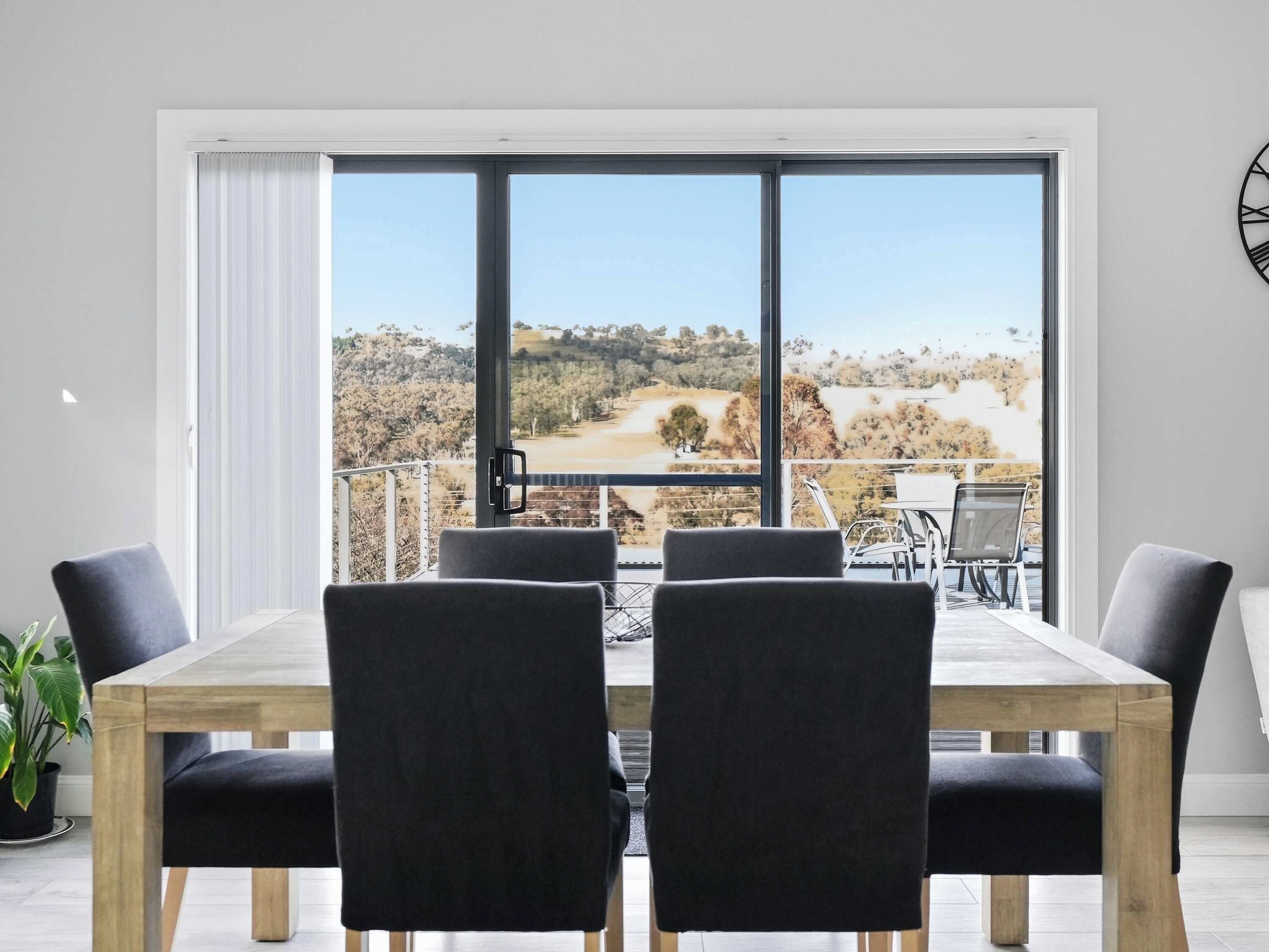 A dining area with a table and chairs, large windows with a view of a landscape, and a clock on the wall.
