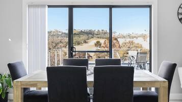 A dining area with a table and chairs, large windows with a view of a landscape, and a clock on the wall.