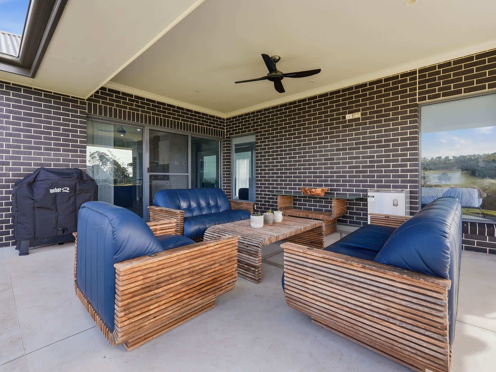 A covered outdoor seating area with a brick wall, a ceiling fan, and a view of the outdoors.