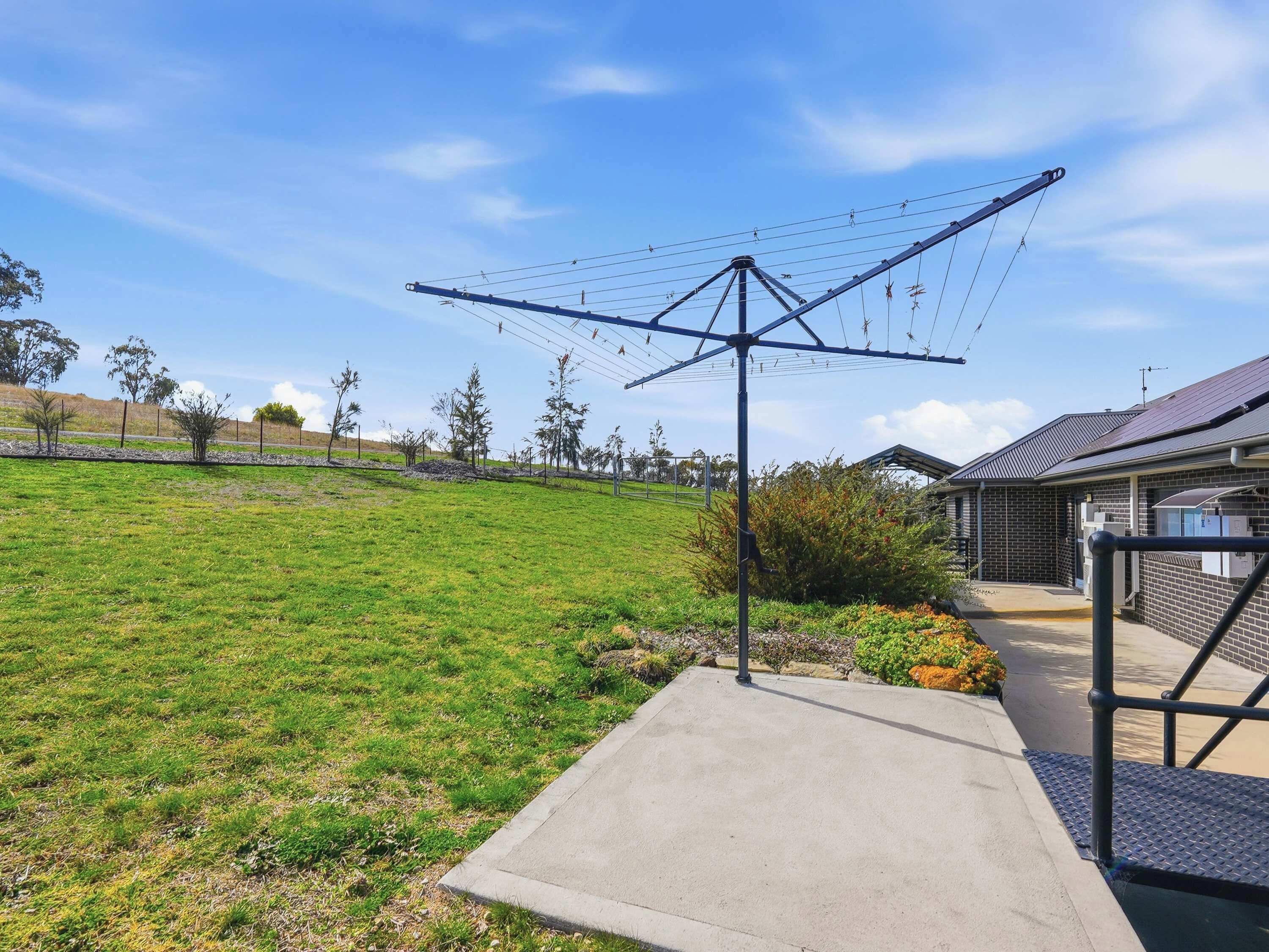 A grassy outdoor area with a concrete pathway leading to a building with a metal staircase.
